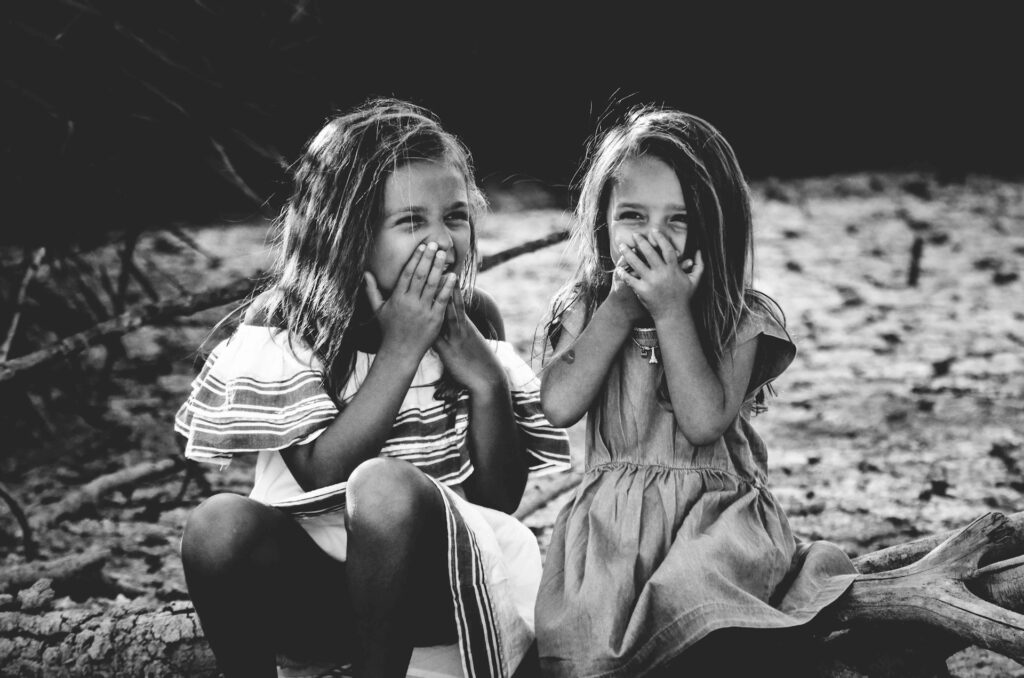 Two young girls laughing covering their mouths with their hands